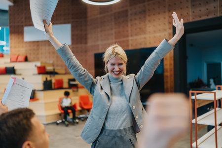 Confident woman celebrates victory in modern office, raising arms and smiling during meeting todayの写真素材