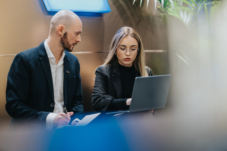 Business professionals discuss project on laptop in a modern office settingの写真素材