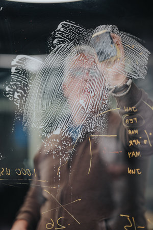 Businessman writes on glass board with fingerprint sketch in modern office environmentの写真素材