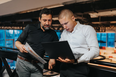 Two professionals review documents and a laptop in a modern, open office setting