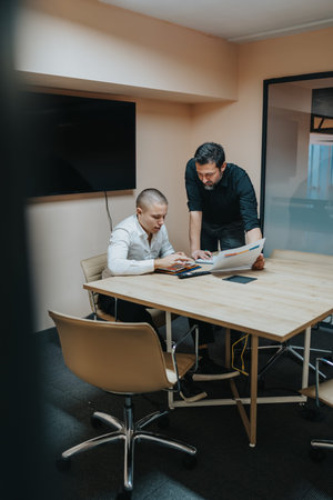 Two professionals collaborate at a conference table with documents and a laptop for business planning.の写真素材