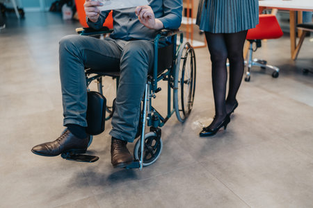 Professional office scene with a wheelchair user and standing colleague in a modern workspaceの写真素材
