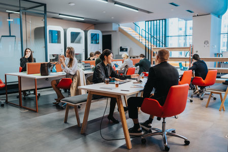 Busy modern coworking space with professionals working on laptops at shared tables and red chairs