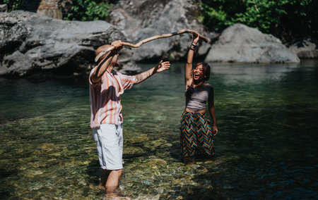 Two friends playing with a branch in a clear summer river by rocky shore