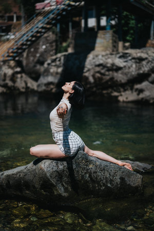 Woman practicing yoga pose on rock by the river in sunny outdoor setting
