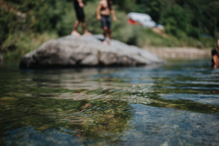 Friends by a sunny river, jumping from a rock on a summer day, enjoying outdoor water fun