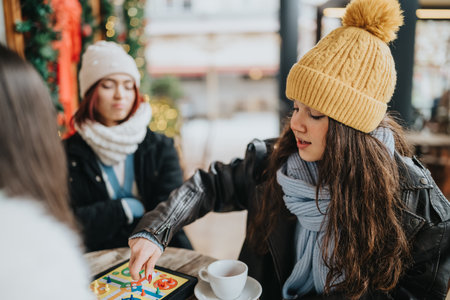 Two girls enjoy a cozy winter cafe moment playing a board game and sharing coffee