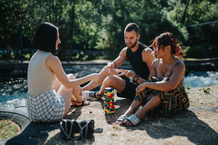 Friends enjoy outdoor summer fun by the water, stacking colorful blocks and laughing togetherの写真素材