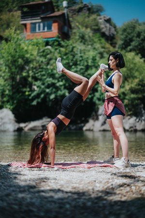 Two friends practice a handstand by the river on a sunny summer day