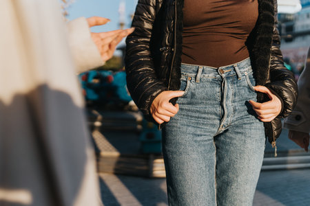 Woman in brown top and black puffer jacket with hands in pockets outdoors during daytime urban scene