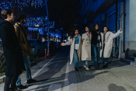 Group of friends walk on city street at night under blue festive lightsの写真素材