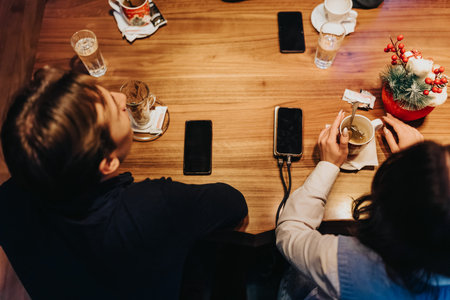 Top view of two people at a wooden cafe table with phones, coffee, and festive decor