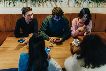 Friends sit around a wooden cafe table, each using a smartphone in a casual gathering.
