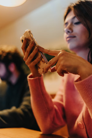 Woman in pink sweater uses smartphone indoors with warm lighting and relaxed expression