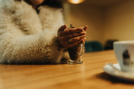 Cozy moment as hands in a furry coat cradle a hot chocolate mug at a cafe table