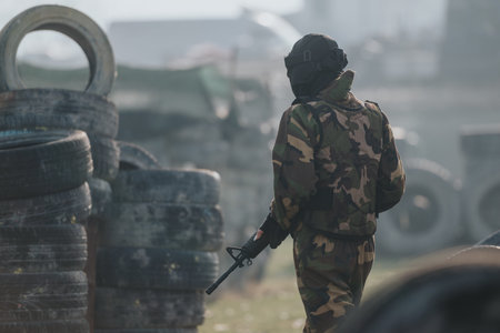 Paintball player in camouflage gear holding a marker in a tire-filled field