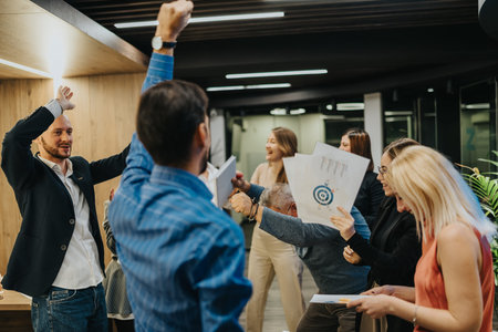 Team celebration in office as colleagues cheer, share documents, and celebrate a project milestone