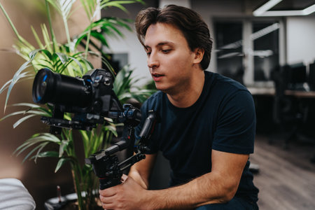 Male videographer operating a camera rig with a stabilizer indoors, focusing on filming