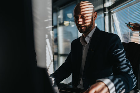 Business man in a professional office setting working at a desk with blinds shadowing his face