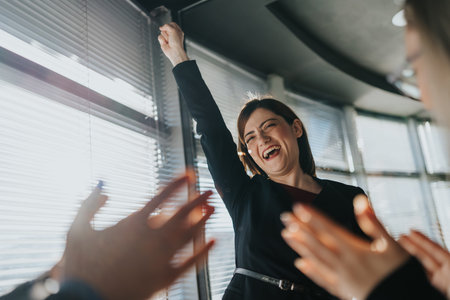 Happy woman raises her arm in celebration as colleagues applaud in a bright office today.