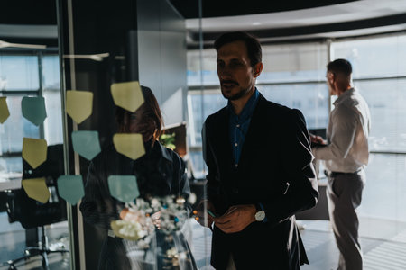 Business colleagues collaborate in modern office with glass wall and sticky notes for planning