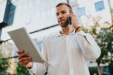 Businessman talking on the phone outside while holding a tablet on a sunny day
