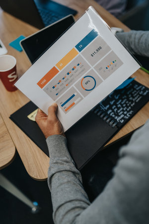 Person reviews printed business charts and graphs on a desk with laptop and notebook