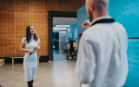 Female presenter in white dress delivers a speech to a man in a lab coat in a modern office setting