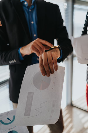 Professional man in a blazer reviews charts and graphs from printed business documents in office