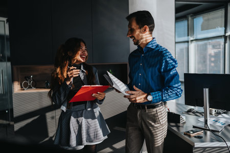 Business colleagues share a smile while discussing documents in a modern office environmentの写真素材