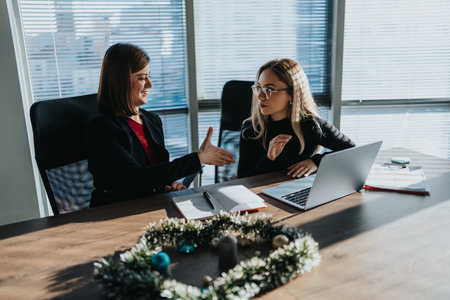 Two professional women discuss ideas in an office during a holiday season meeting