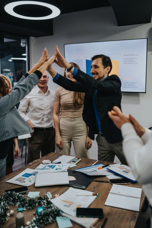 Business team celebrates success with a high-five around a cluttered conference tableの写真素材