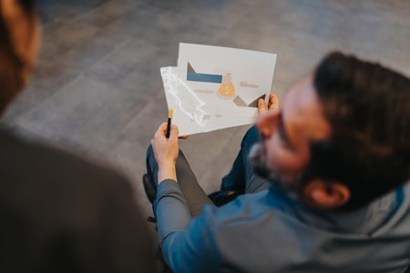 Business meeting scene as two professionals review a finance info graphic and notes during a discussionの写真素材