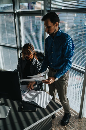 Business professionals collaborate at a desk, reviewing documents and analyzing reports in a modern...