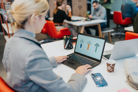 Woman working on laptop in a modern coworking space with info graphic on screen during a busy day