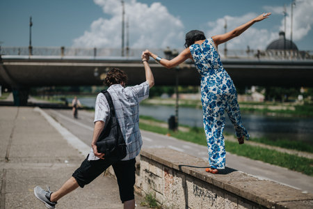 Friends share a playful moment as one person jumps from a ledge beside a river park