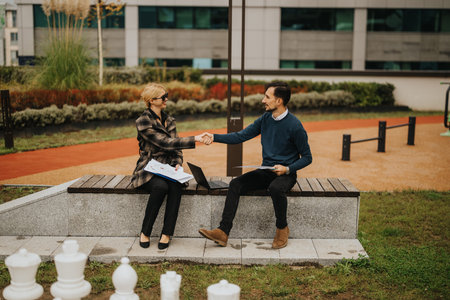 Business partners shake hands on a bench outdoors after a meeting in a modern campus setting