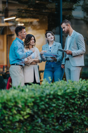 Business group discusses documents outside a modern office building during a casual meeting