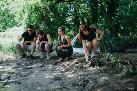 Group of friends camping in the forest, crouching by a tent and campsite together