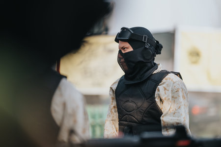 Paintball player in tactical vest and mask preparing for action on outdoor field during game