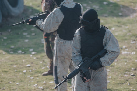 Paintball players in camouflage gear with tactical vests and masks aiming their guns on a field