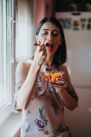 Young woman eating fresh fruit from a glass bowl by a sunny window