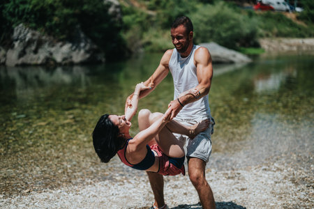 Happy couple enjoys playful riverfront moment as man lifts woman during summerの写真素材