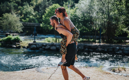Happy friends enjoy a summer day with a piggyback ride by the riverの写真素材