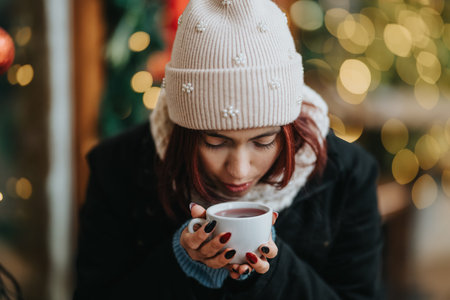 Girl in a knit hat holds a mug of hot drink in a cozy winter setting with festive lights