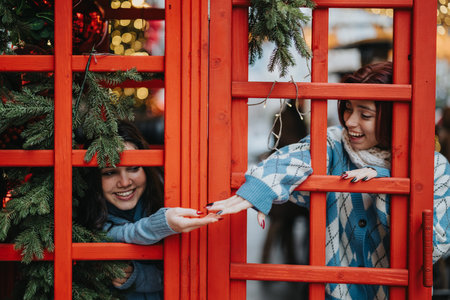 Two teenage girls share a festive moment through a bright red wooden gate during Christmas