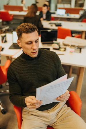 Focused man reading documents in a modern open office with desks and laptops