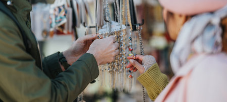 Diverse tourists browsing handmade jewelry at an outdoor market stall on a chilly day