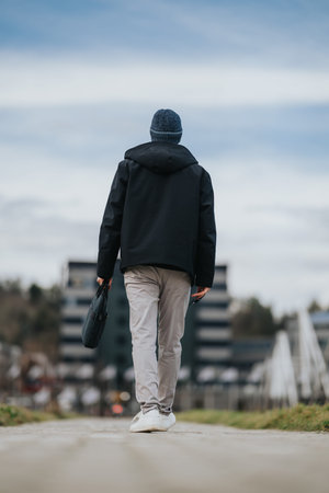 Man walking away on a city sidewalk carrying a bag in casual commuter outfitの写真素材