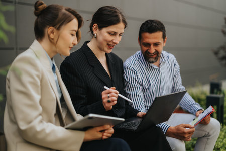 Business collaboration between three professionals reviewing laptop and tablet during an outdoor...